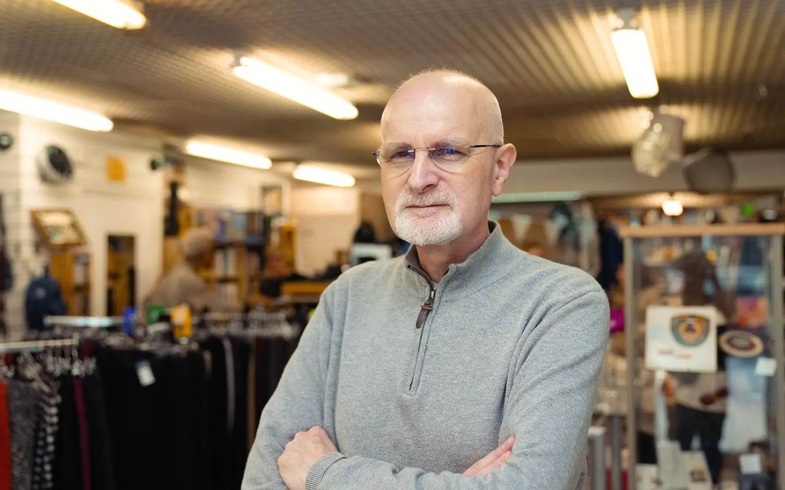 A shop owner standing with his arms folded in his store