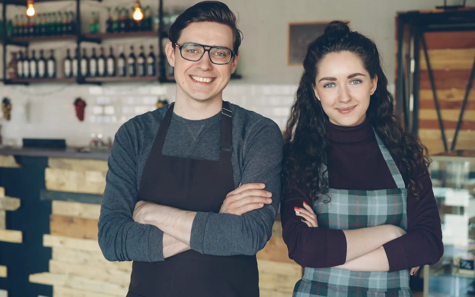 Two café owners in aprons standing together in their shop