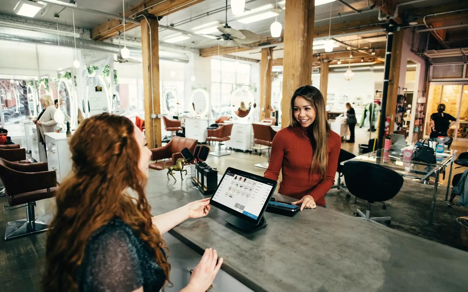 A customer checking out at a tablet point of sale on a busy salon counter