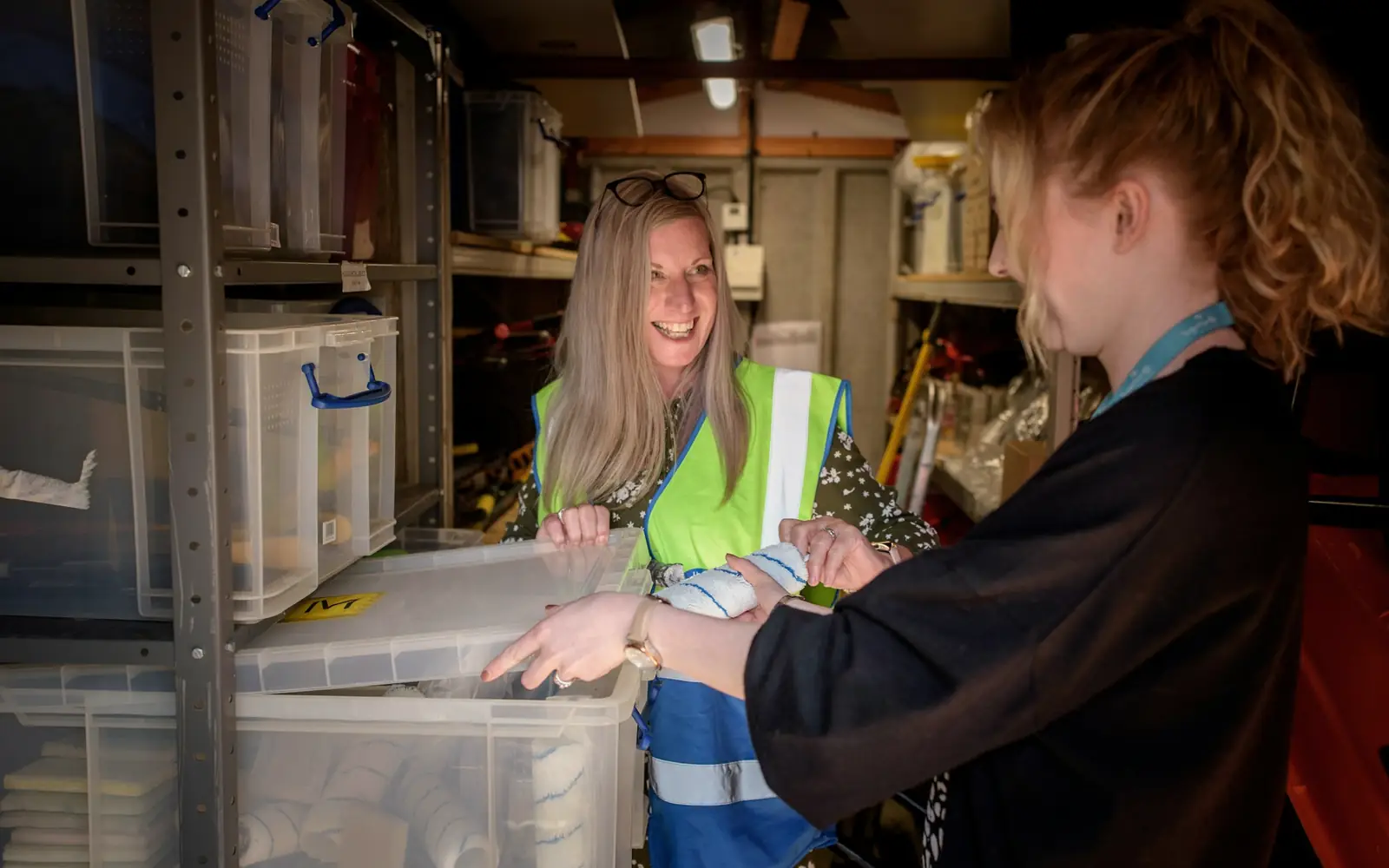 Two colleagues checking items from a storage box in a stockroom