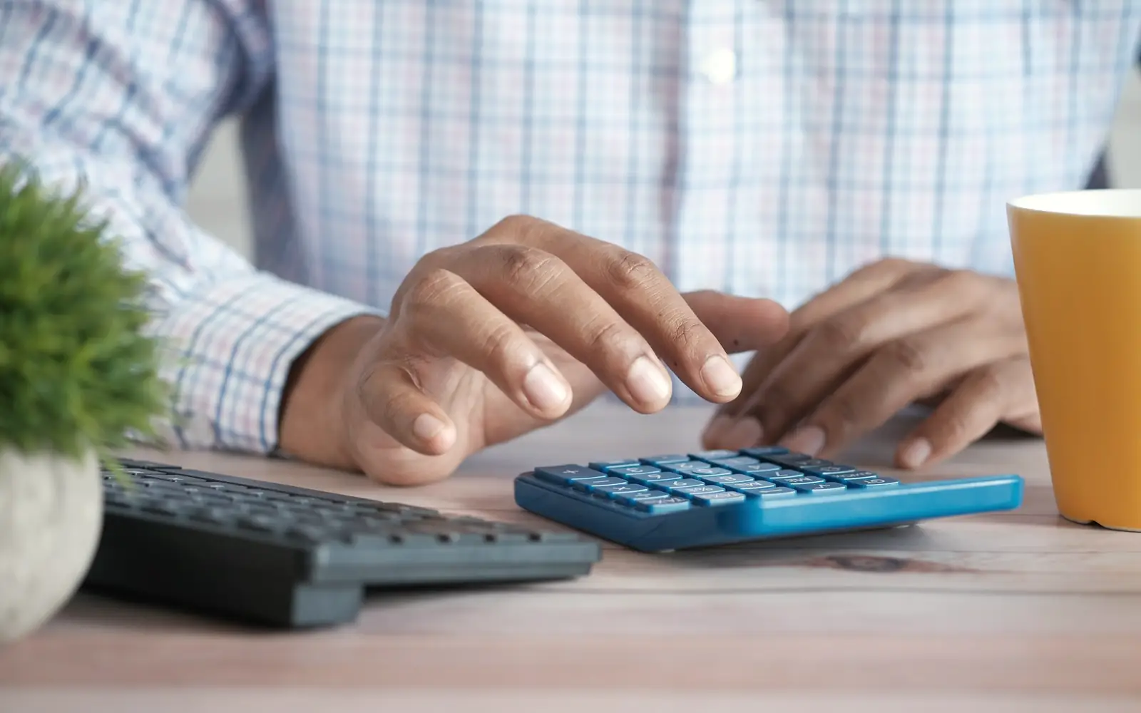 Hands using a calculator beside a keyboard on a desk