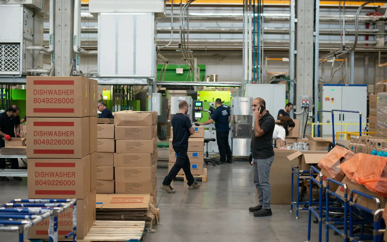 A man standing beside stacked cardboard cartons in a busy warehouse