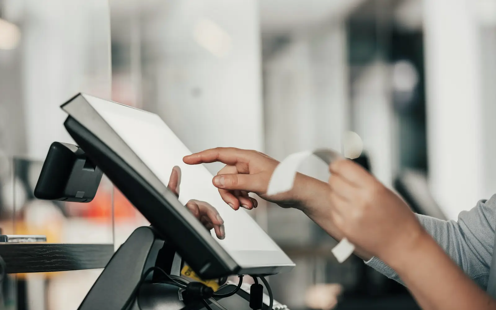 A cashier tapping a point-of-sale screen at a shop counter