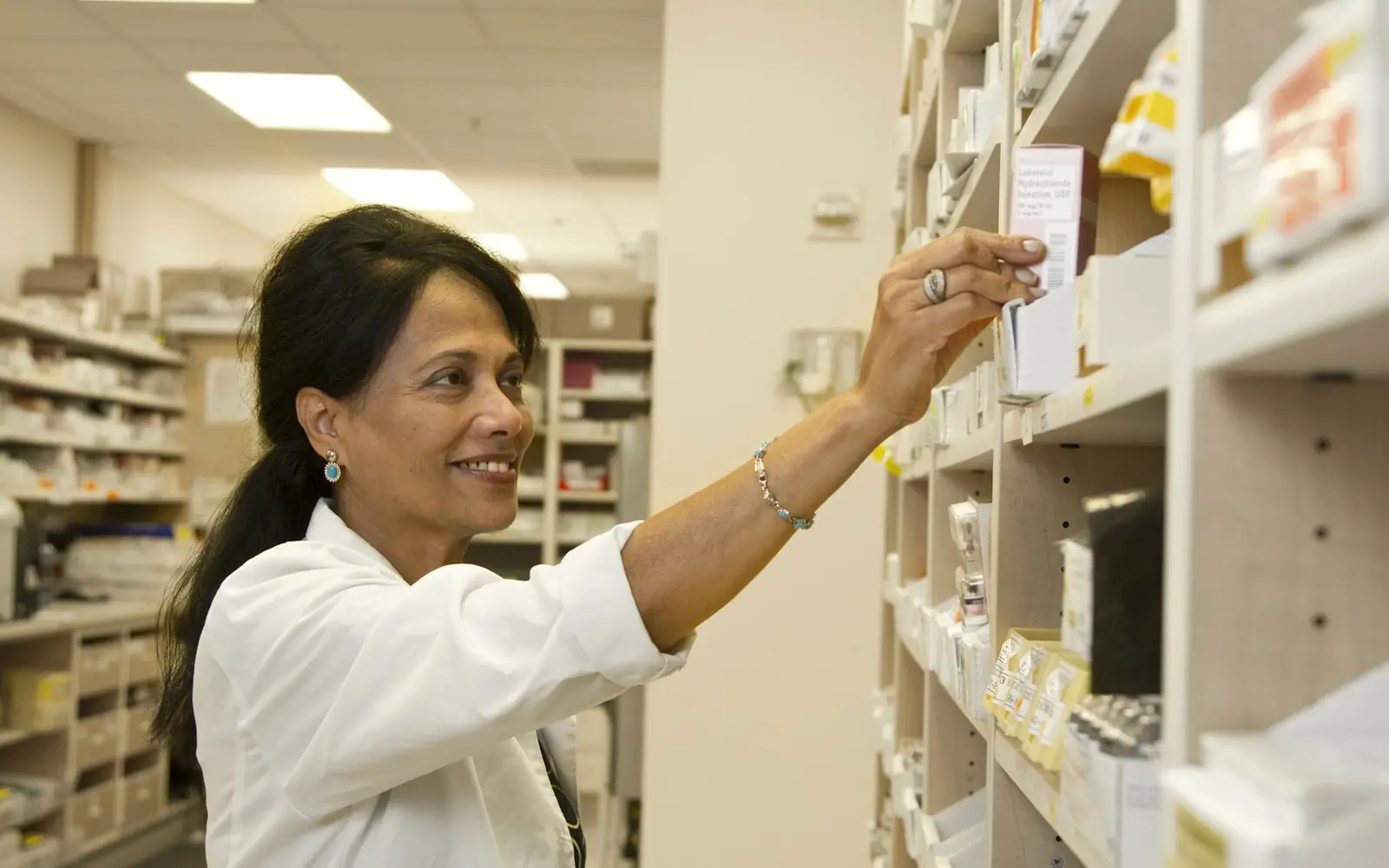 A pharmacist reaching for a box of medication on a pharmacy shelf