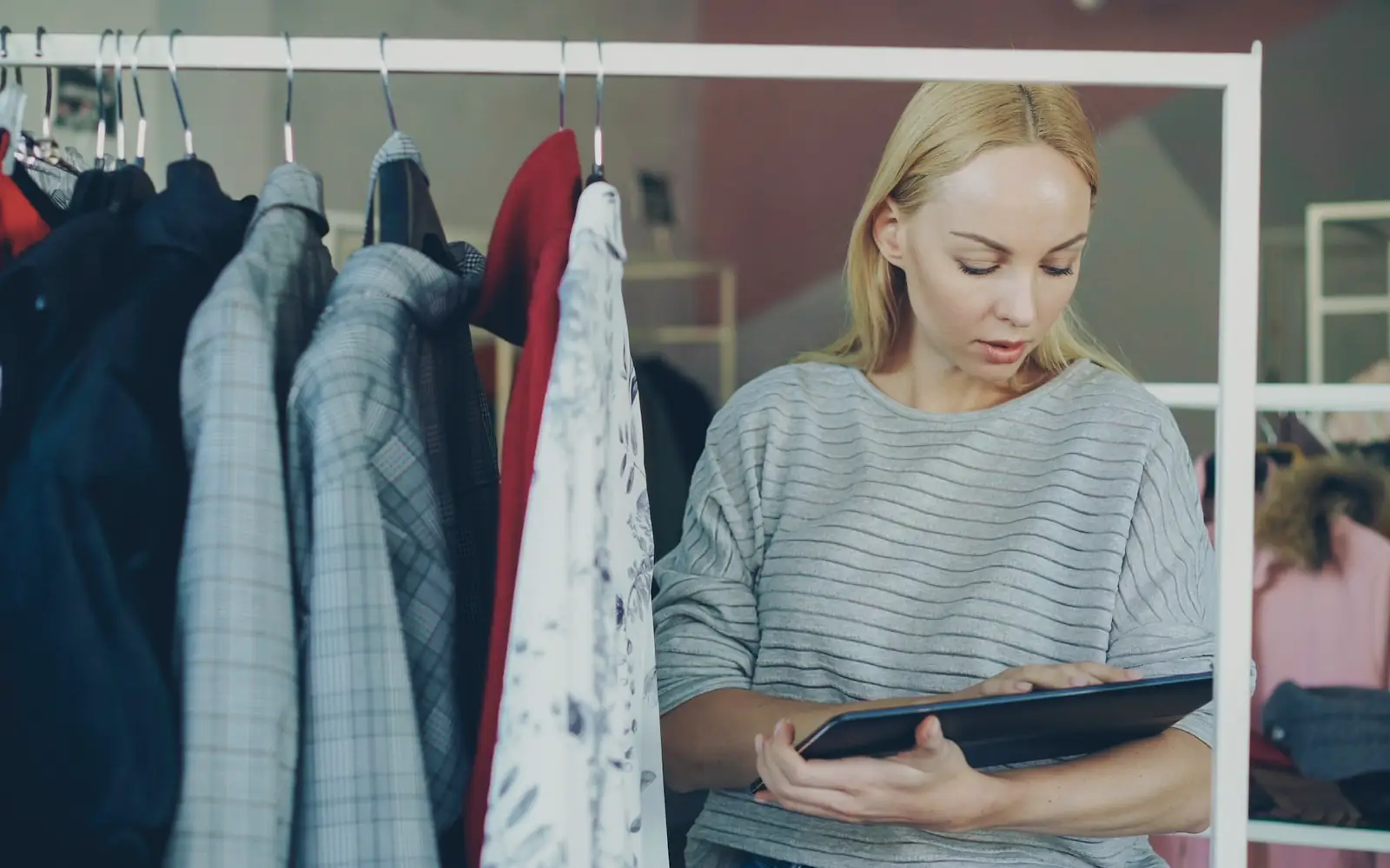 A clothing store owner checking stock on a tablet beside a rail of garments