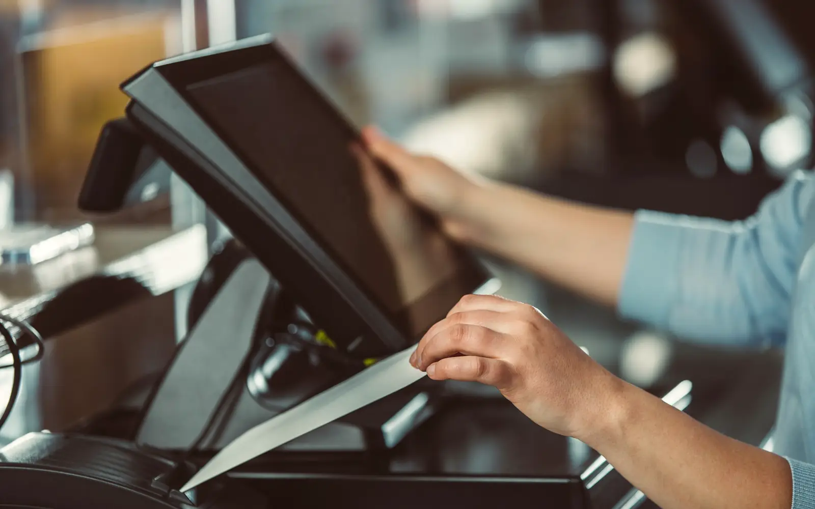 A cashier tapping a point-of-sale screen as a receipt prints