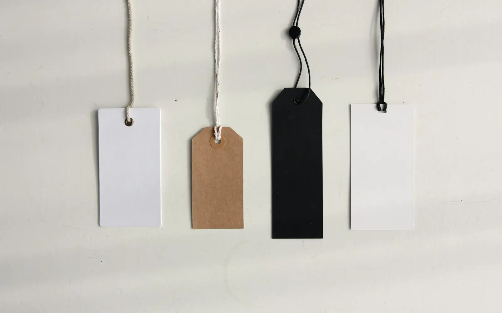 Four blank price tags hanging on strings against a pale wall