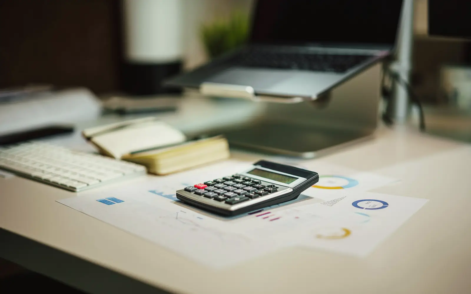 A calculator on printed financial reports beside a laptop